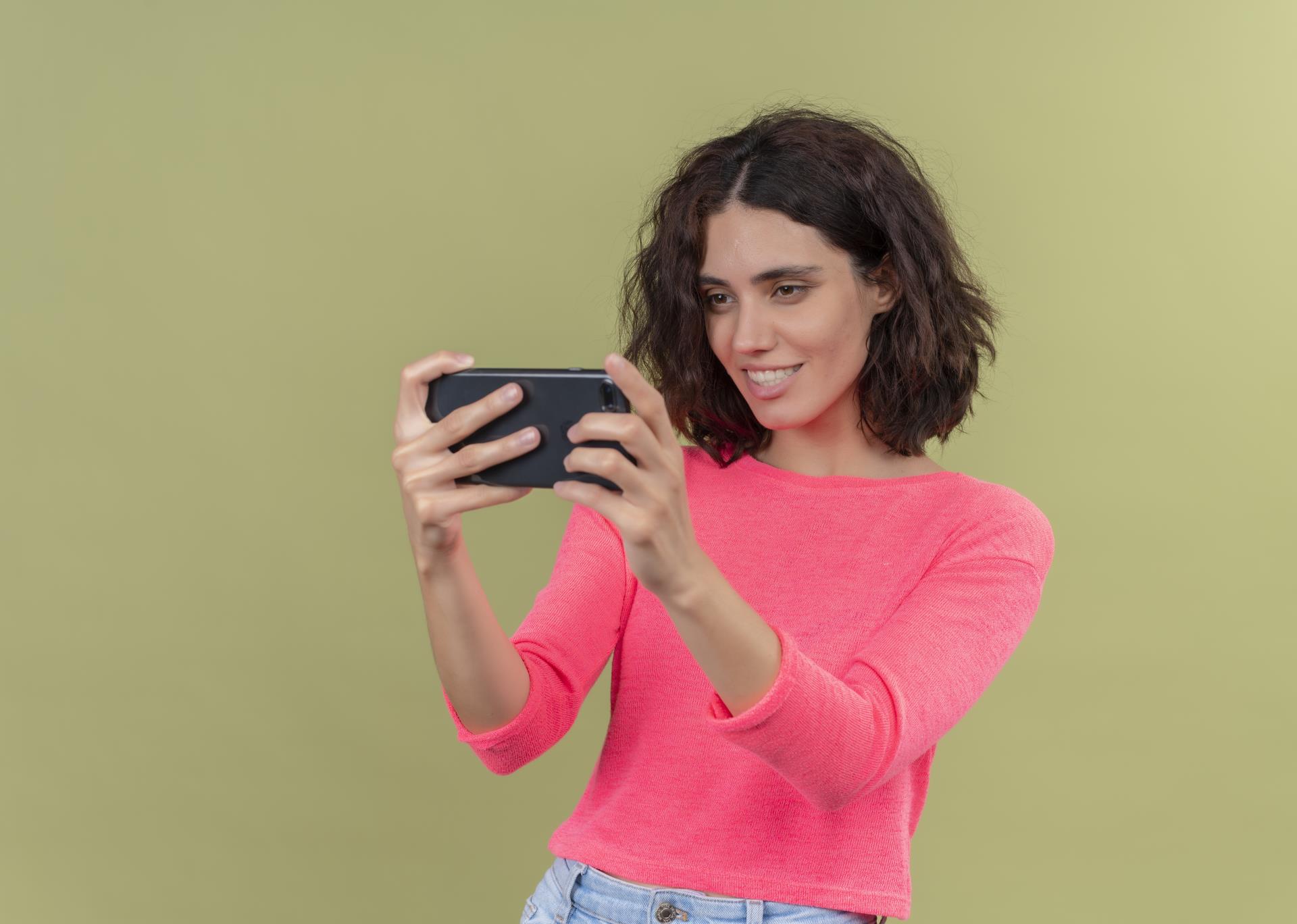 smiling-young-beautiful-woman-holding-mobile-phone-looking-it-isolated-green-wall