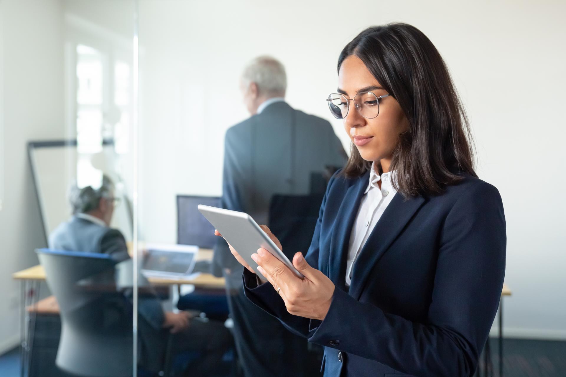 focused-office-lady-glasses-using-tablet-while-two-mature-businessmen-discussing-work-glass-wall-copy-space-communication-concept