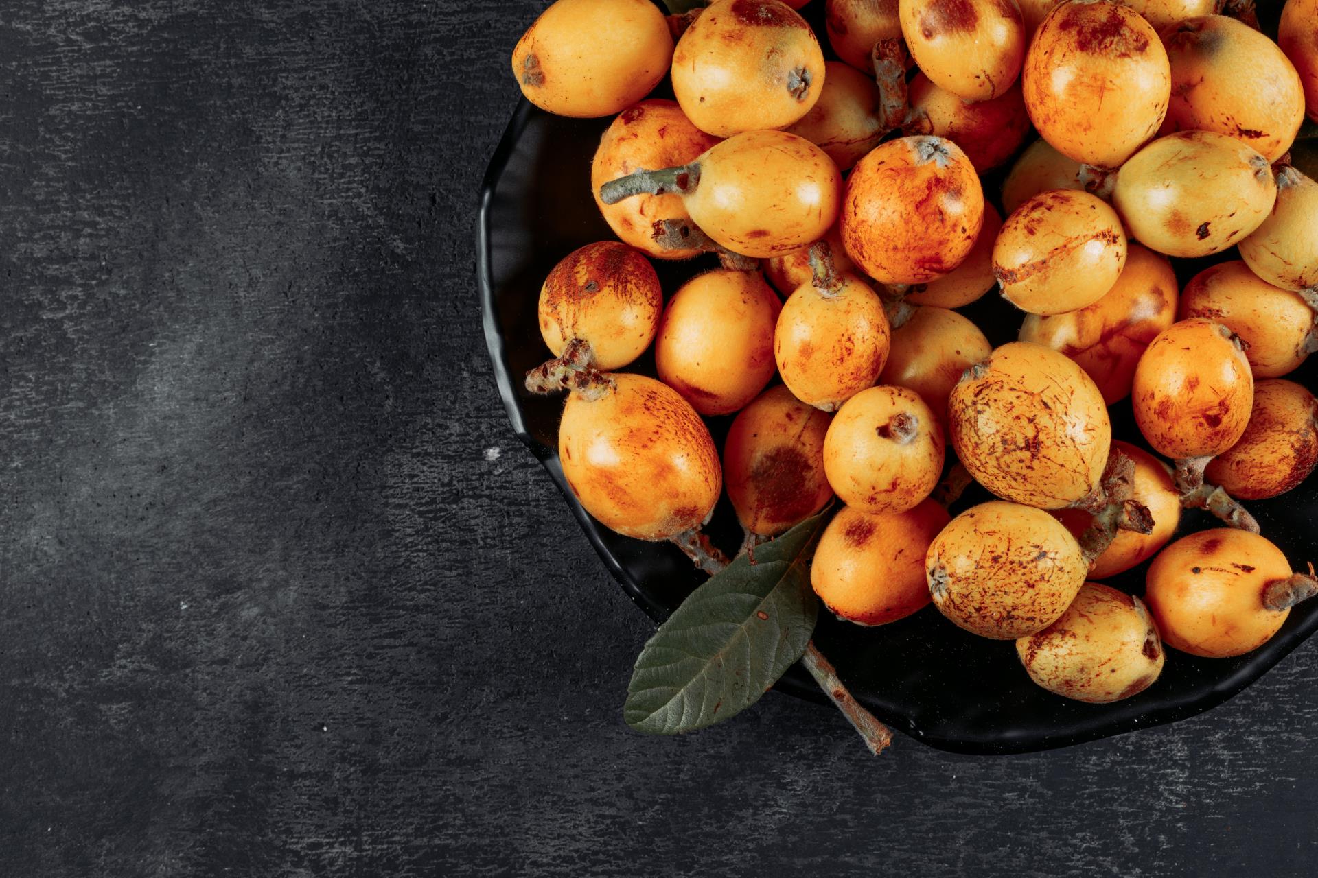 top-view-loquats-bowl-with-leaves-dark-textured-background-horizontal