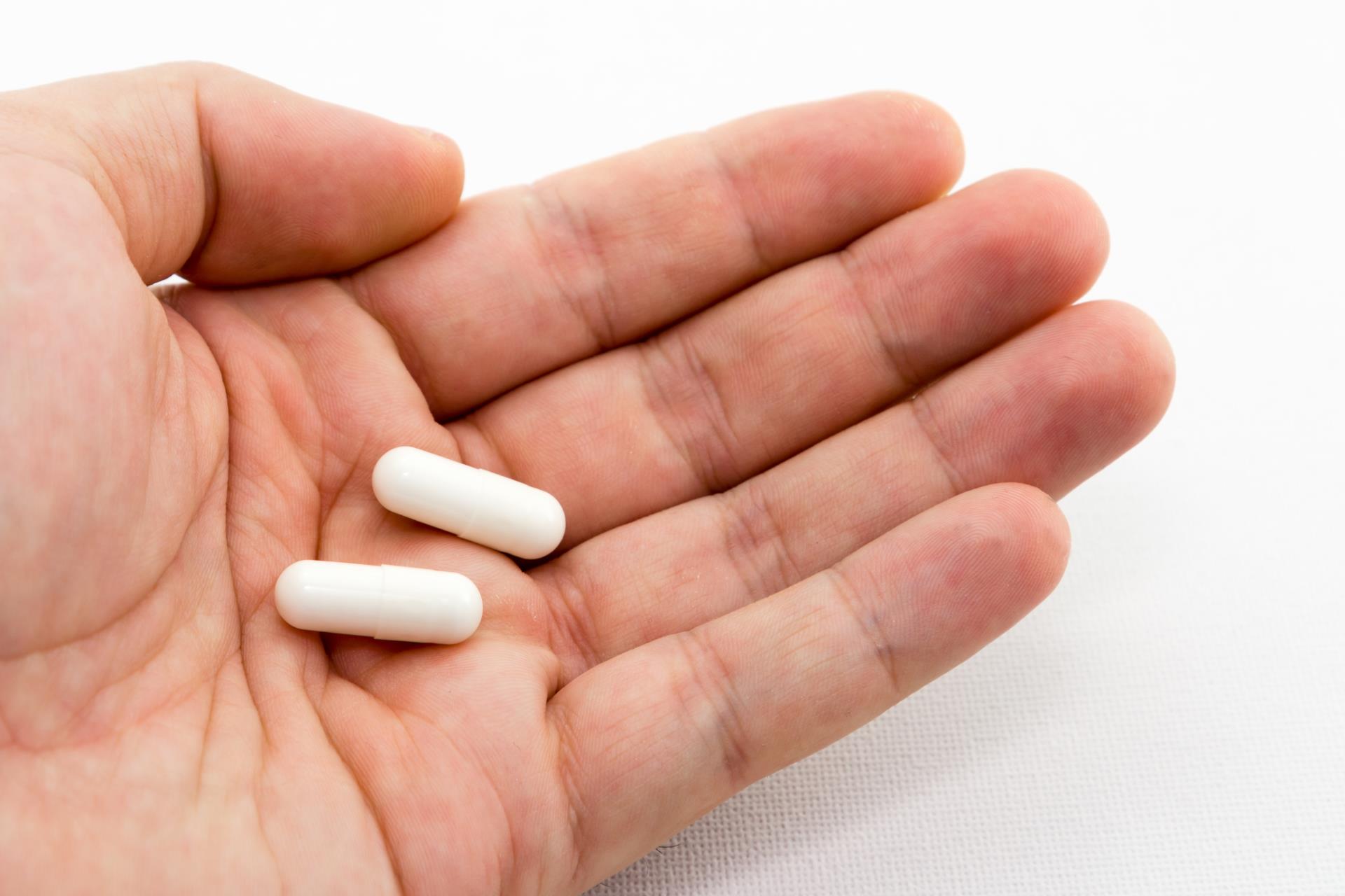 closeup-shot-person-holding-two-white-capsules