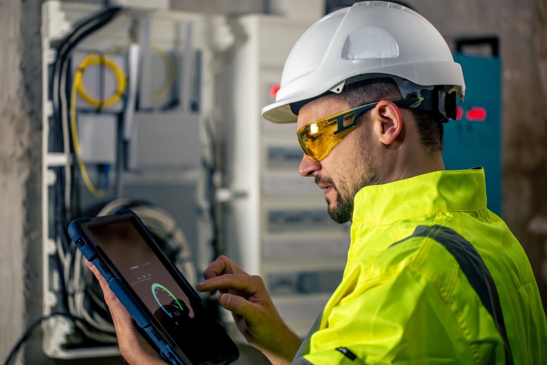 man-electrical-technician-working-switchboard-with-fuses-uses-tablet