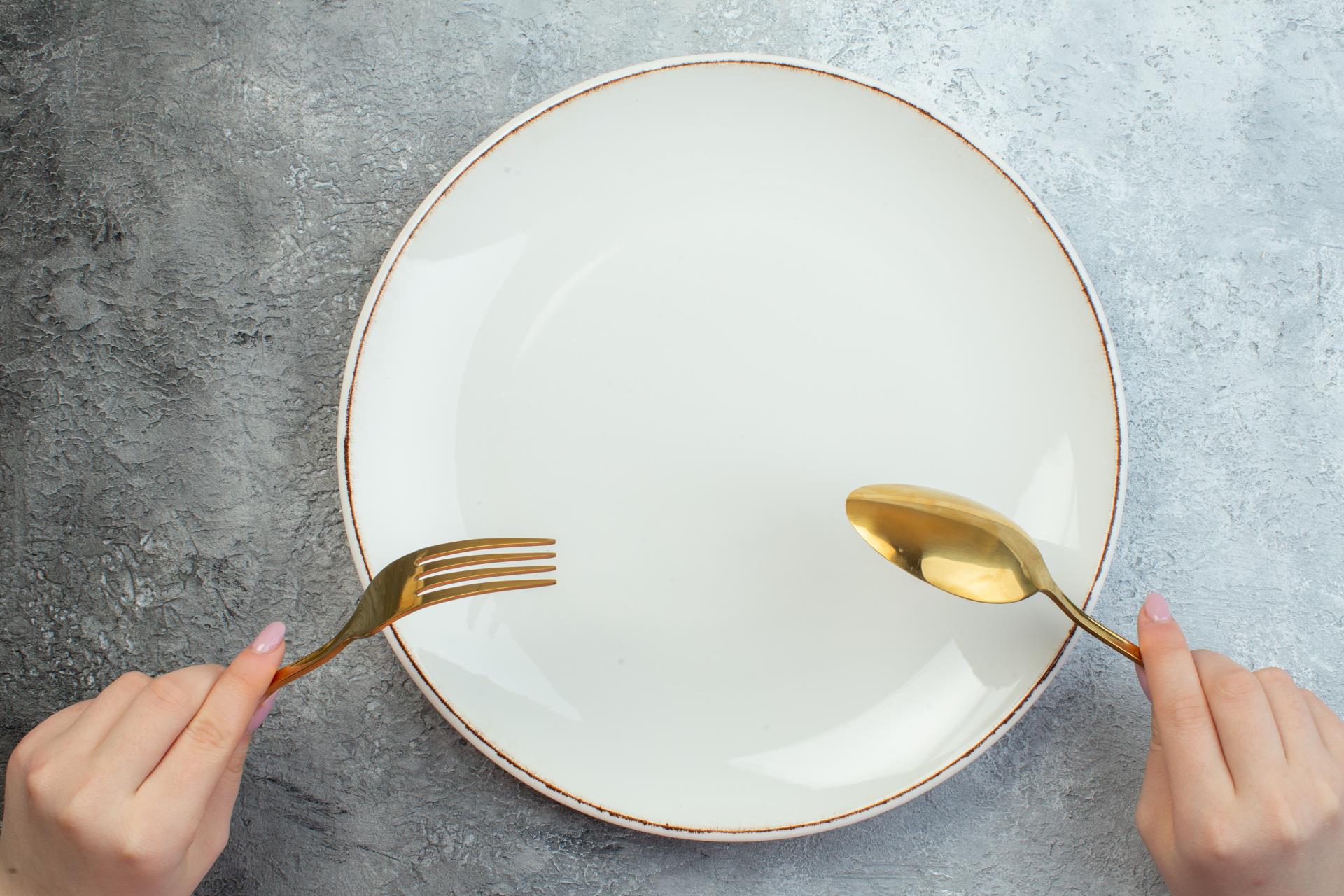 woman-hand-holding-cutlery-set-empty-plate-gray-surface