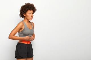 profile-shot-afro-american-female-model-suffers-from-stomachache-has-abdominal-pain-touches-belly-wears-top-shorts-frowns-face-from-unpleasant-feelings-poses-against-white-background