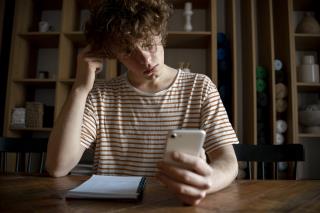 young-man-writing-something-notebook-while-looking-his-smartphone (1)